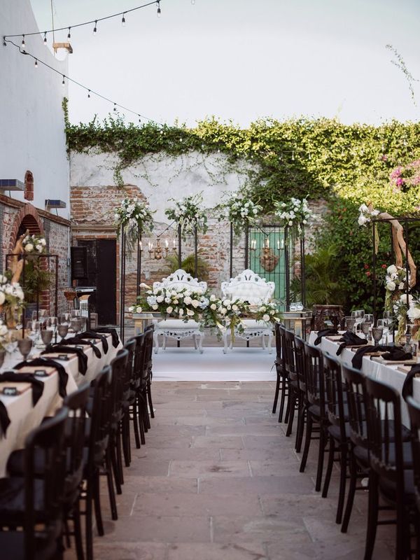 Long reception tables set with candles and flowers in an ivy-covered courtyard under string lights